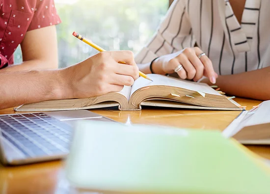 two people marking something on a book using a pencil